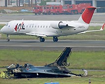事故から一夜が明け、無残な姿をさらす航空自衛隊の戦闘機(手前)と、運用が再開された滑走路を飛び立つ航空機=1日、愛知県豊山町〔共同〕